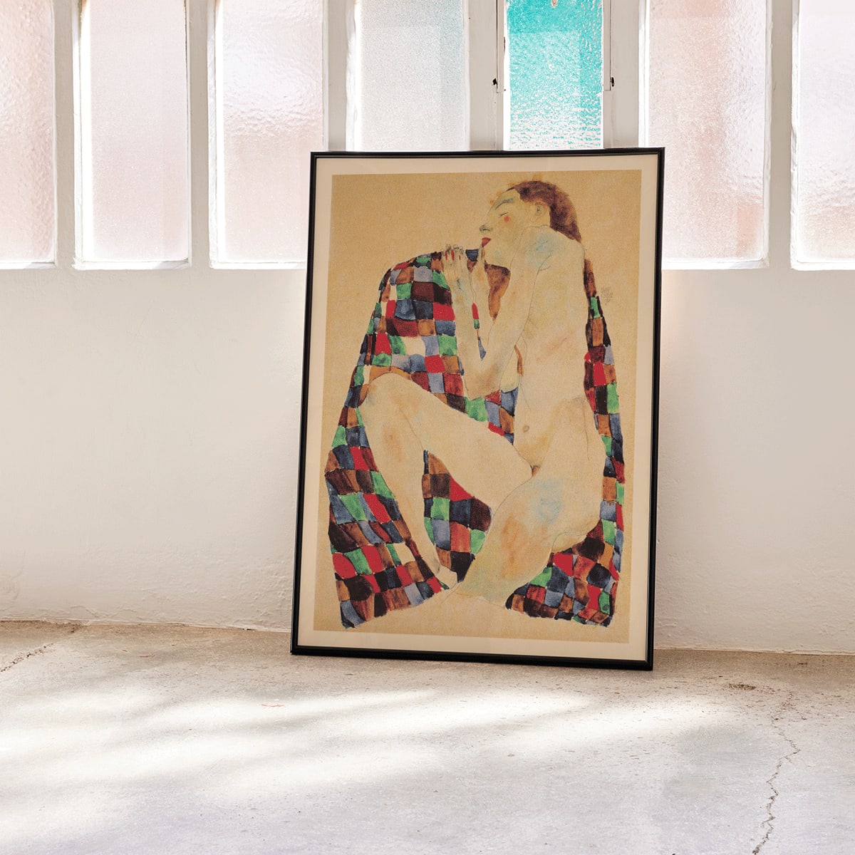Female Nude on Checkered Cloth by Egon Schiele showing a nude woman sitting on a colorful patterned fabric poster, framed and displayed in home decor